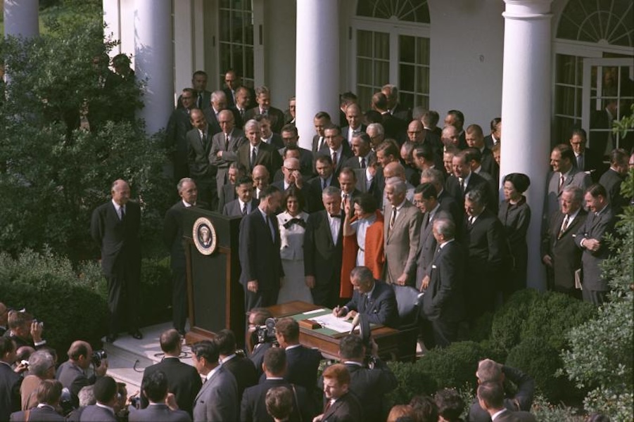 President LBJ signing Arts and Humanities Act surrounded by a crowd of people. 