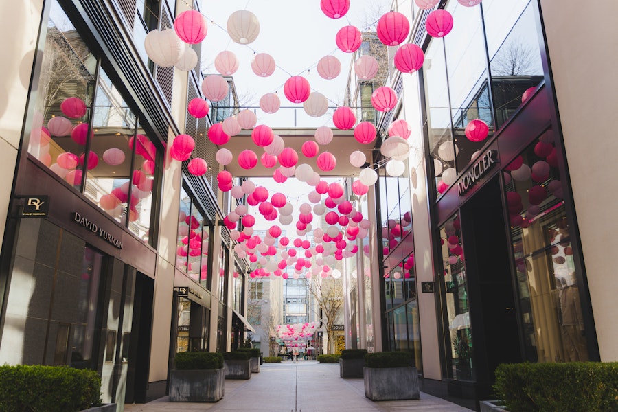Pink lanterns decorate a modern alleyway lined with chic storefronts. 