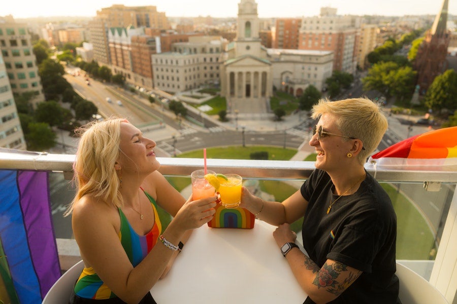 A couple enjoying a cocktail on a rooftop with a view of historic city buildings below. 