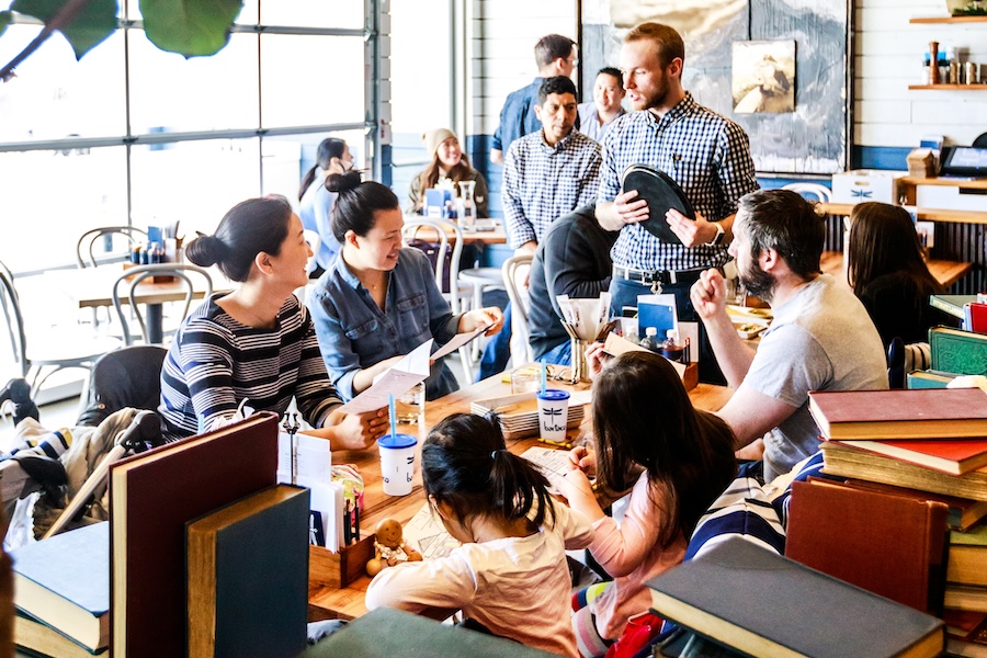 A family with young kids comfortable sits around a restaurant table while a server takes their orders. 