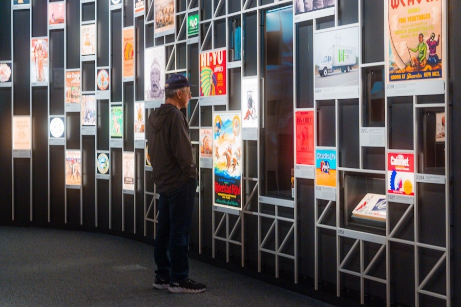 A man studies colorful vintage posters arranged on a modern grid wall display at the National Museum of the American Indian.
