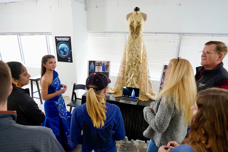 A group looks at a display with a futuristic-looking dress. 