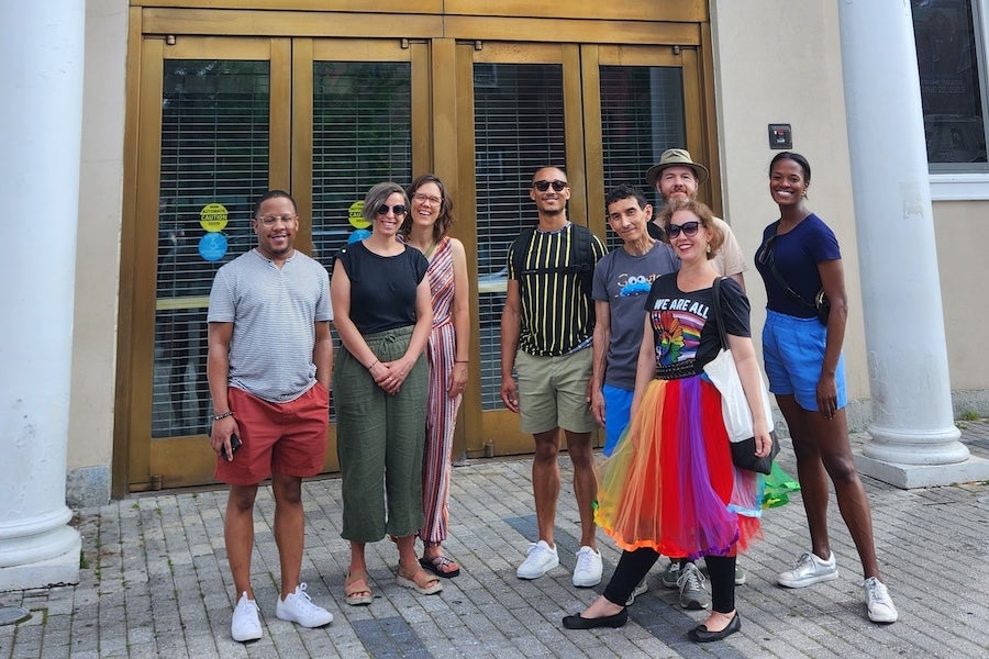 A group smiles for a photo outside a historic theater in Washington, DC with a guide in a rainbow skirt. 