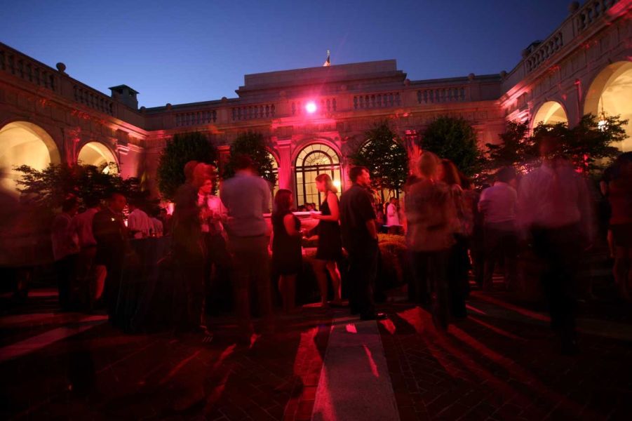 Group of people dancing in a museum with one red spotlight in a courtyard