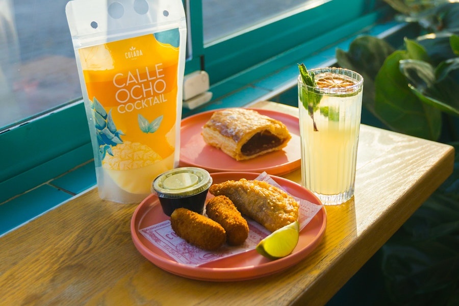 A table set with Cuban snacks, a cocktail pouch and a fresh lime drink at Colada Shop.