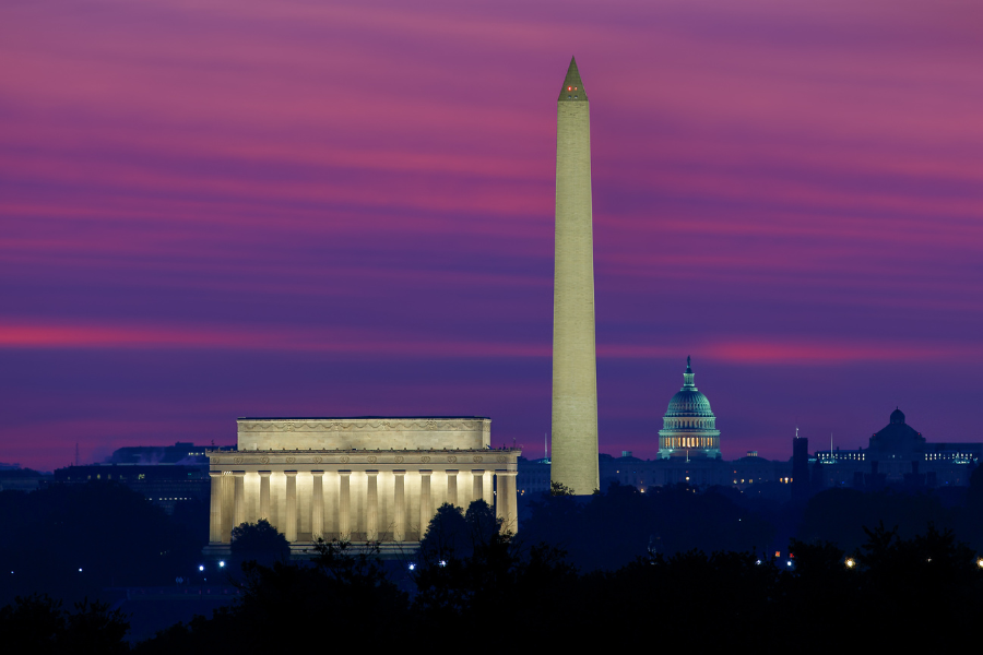 The Lincoln Memorial, Washington Monument, and U.S. Capitol glow against a dramatic purple and pink dusk sky in Washington, DC.