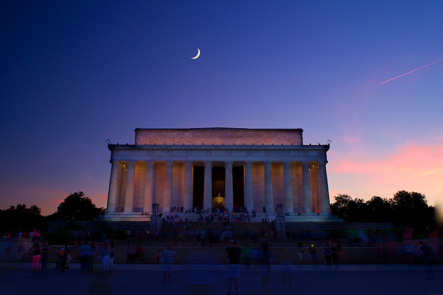 The Lincoln Memorial illuminated under a twilight sky with a crescent moon overhead.