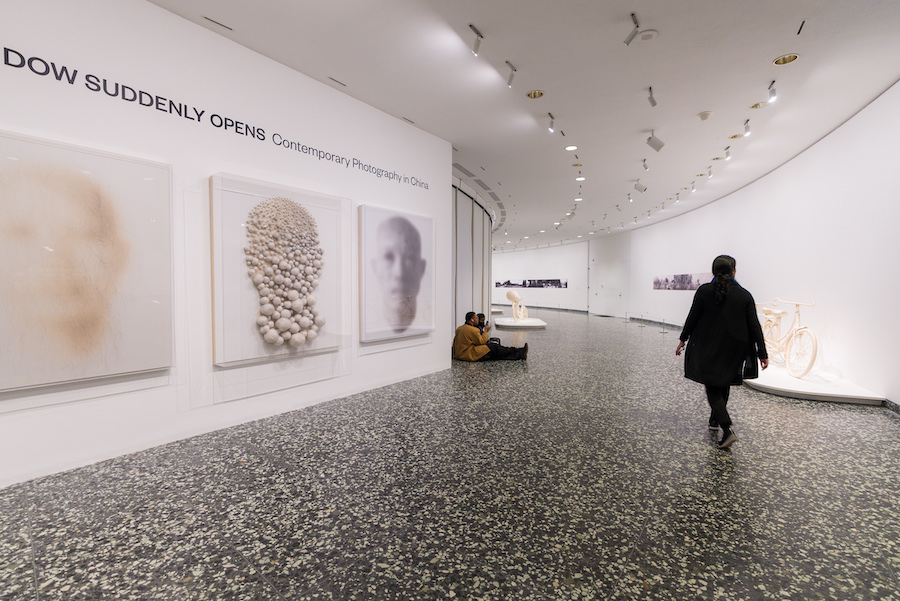 Visitors explore “A Window Suddenly Opens: Contemporary Photography in China” at the Hirshhorn Museum in Washington, DC, featuring large-scale portraits and minimalist sculptures.