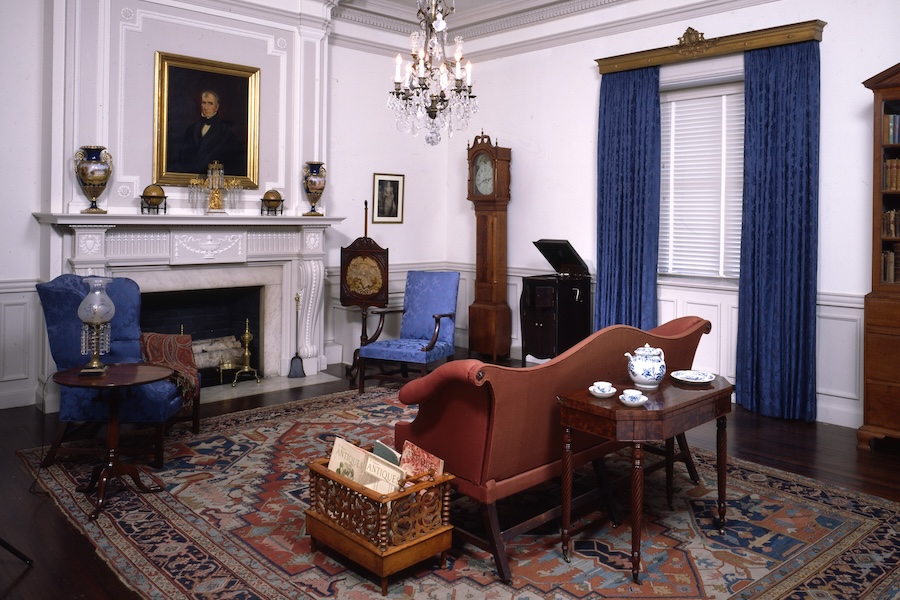 A historic parlor room exhibit at the DAR Museum featuring antique furnishings, a crystal chandelier, a white fireplace with decorative vases, and a portrait above the mantel.