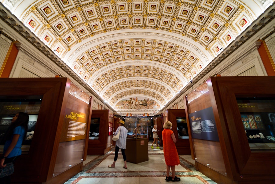 Visitors explore an ornate exhibition hall in the Library of Congress with a richly decorated arched ceiling and museum displays.