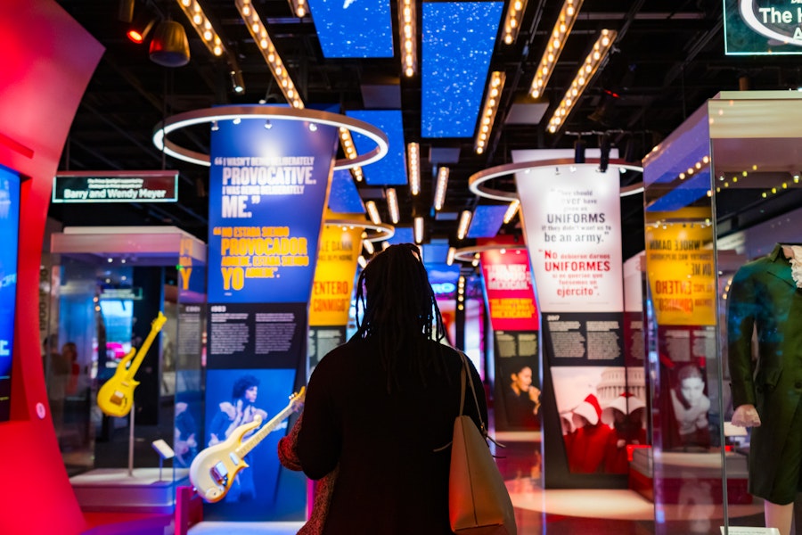 A visitor walks through a colorful and immersive exhibit at the National Museum of American History, featuring guitars, quotes and historic pop culture displays.