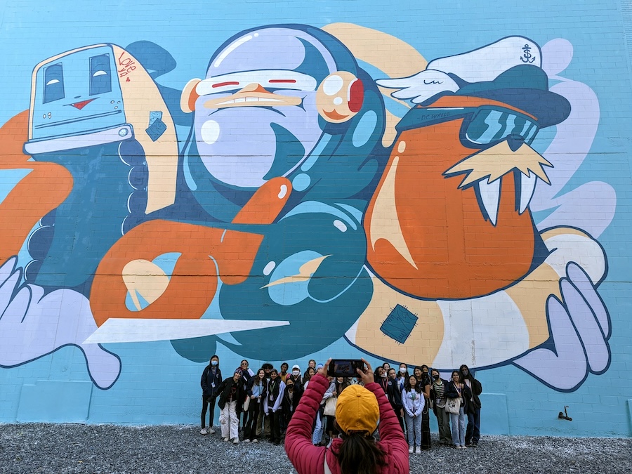 A colorful mural with cartoon-like characters and a group of visitors posing in front of it in Washington, DC’s NoMa neighborhood.