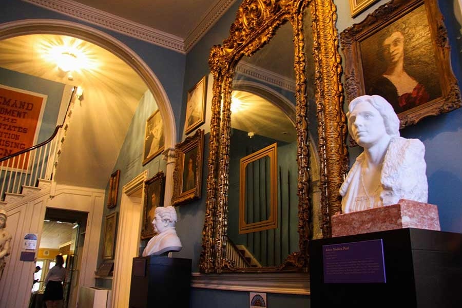 The Hall of Portraits in the Belmont-Paul Women's Equality National Monument. Busts of Alice Paul and Elizabeth Cady Stanton are displayed on pedestals. Portraits on the walls represent many National Woman's Party members