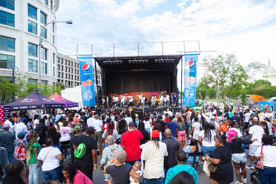 A large crowd gathers in front of a festival stage for a live performance downtown.