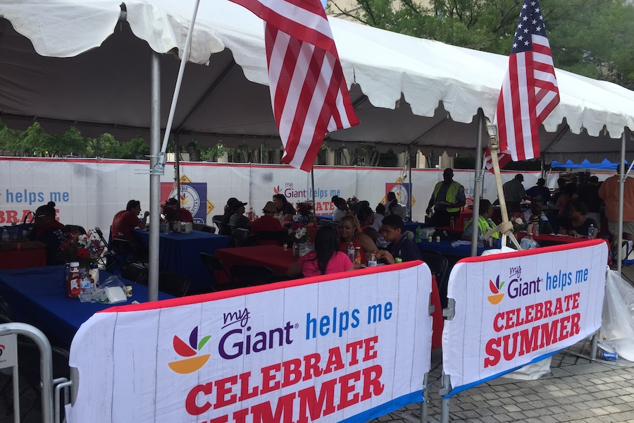 Families gather under a decorated tent with American flags to enjoy food and festivities.