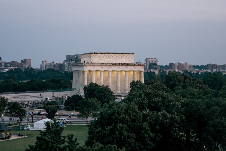 The Lincoln Memorial is illuminated at dusk with the city skyline visible in the distance.