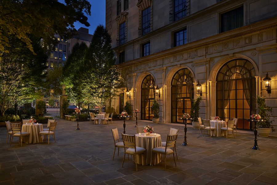 An elegant outdoor courtyard is set with candlelit tables outside a historic building at dusk.