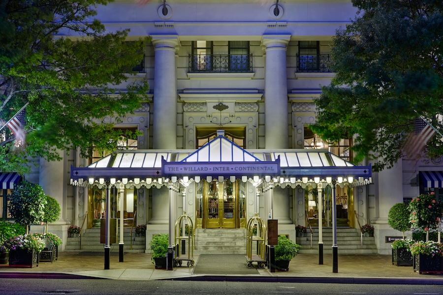 The Willard InterContinental’s illuminated entrance glows at night beneath a classic canopy and columns.