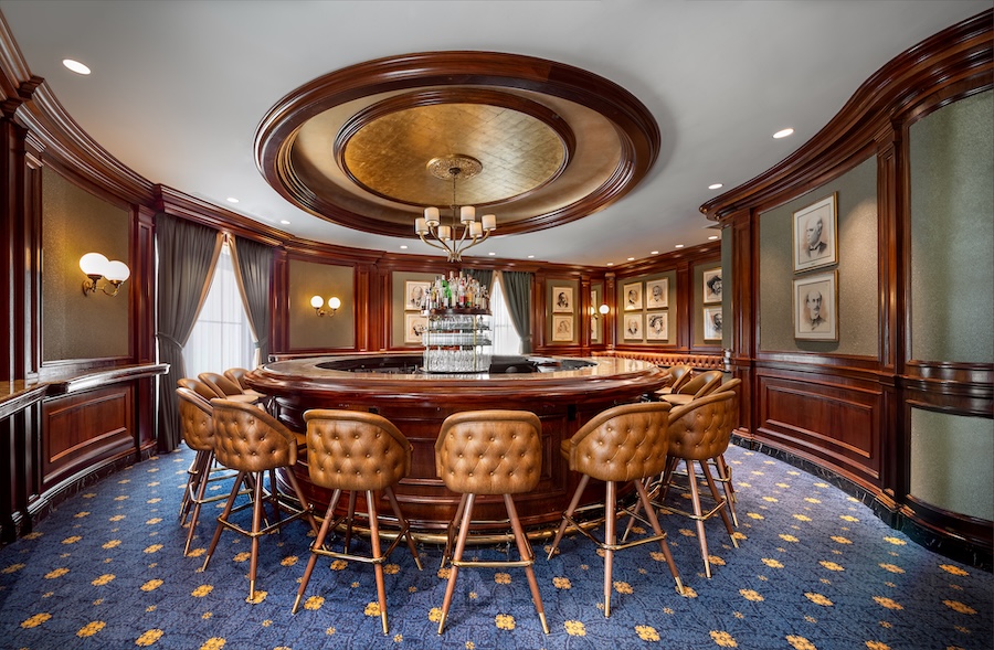 The historic Round Robin Bar features a circular wooden bar surrounded by tufted leather stools and rich wood paneling. 