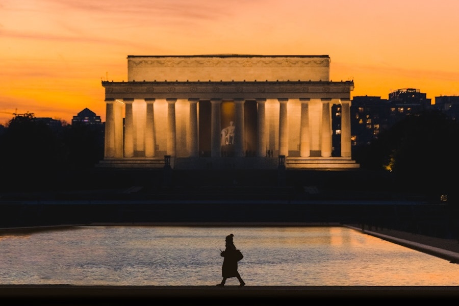 Silhouette of a person walking by the Lincoln Memorial at sunset, reflecting pool in front