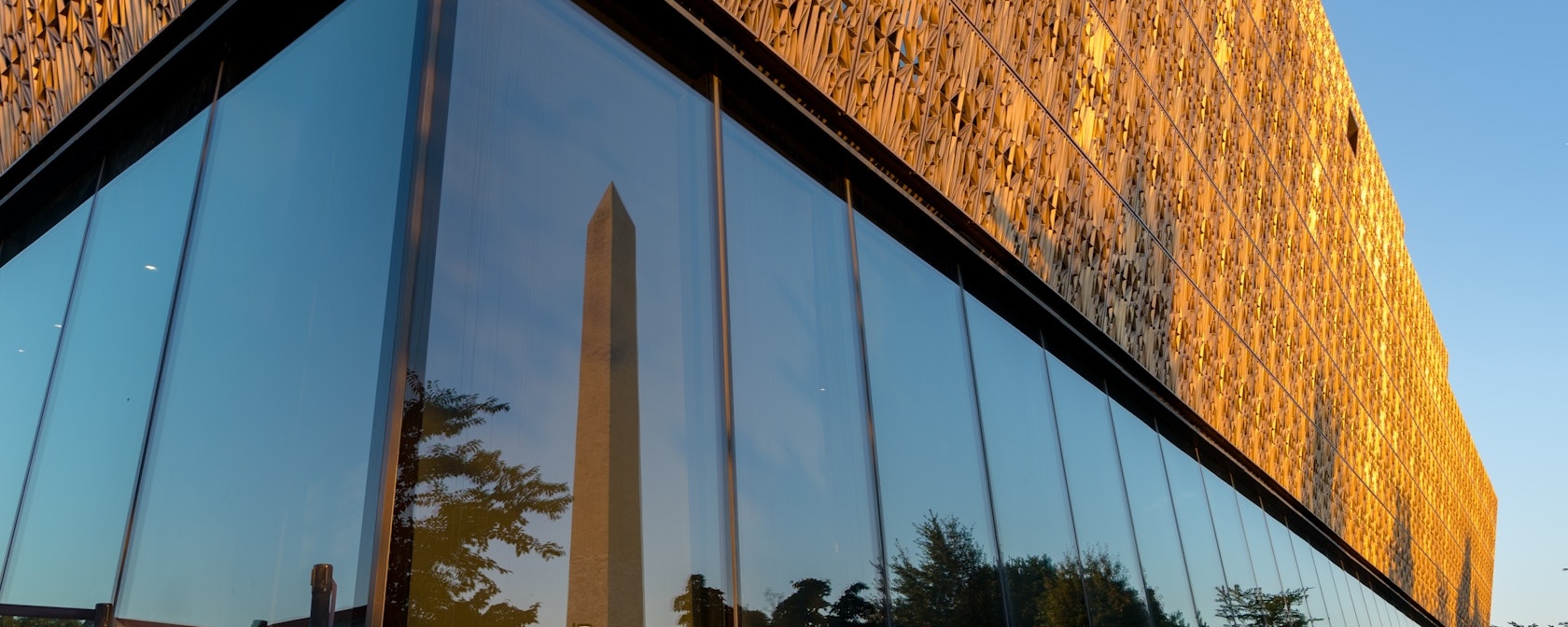 Modern glass building with obelisk reflected, golden facade in evening light