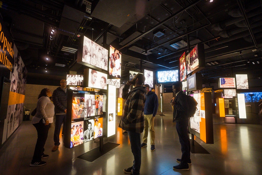Visitors viewing illuminated displays in a dimly lit museum gallery.