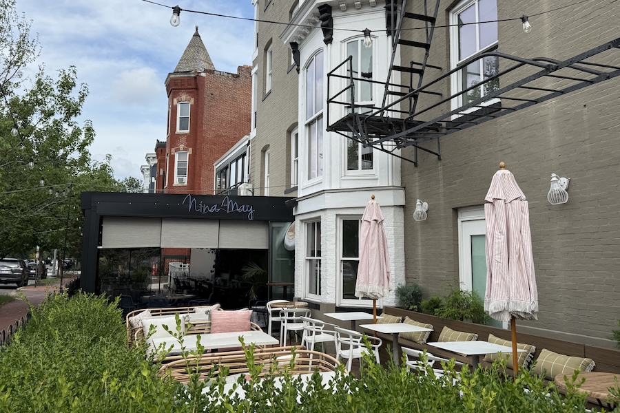 Outdoor patio with tables, chairs and closed umbrellas beside a building
