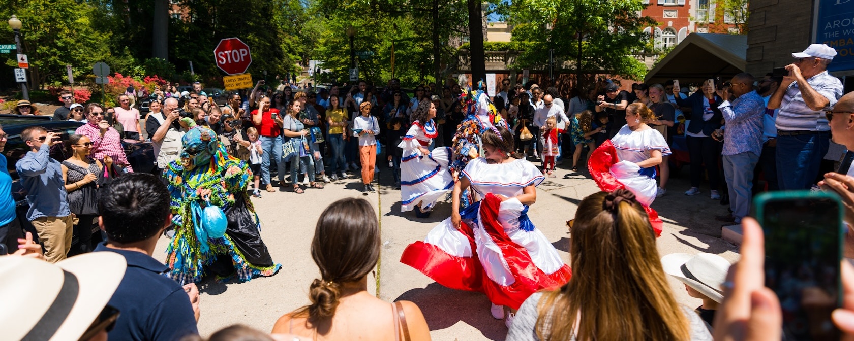 Crowd watches performers in red, white, and blue costumes at an outdoor parade