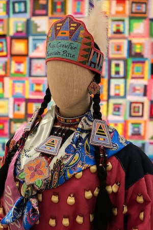 Mannequin in ornate traditional costume and embroidered hat before colorful patterned backdrop