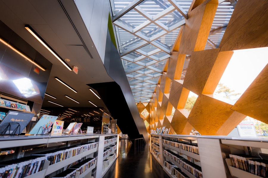 Wide library aisle with bookshelves under geometric skylights and patterned ceiling