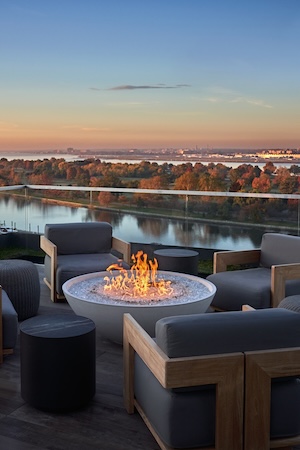 Rooftop seating with a gas fire pit overlooking a river at sunset