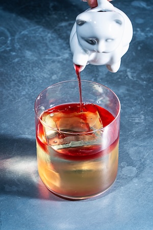 White ceramic cat pouring red liquid into a clear glass candle on a blue surface