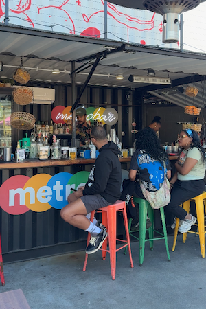 People seated on colorful stools at a metro café counter with hanging lights