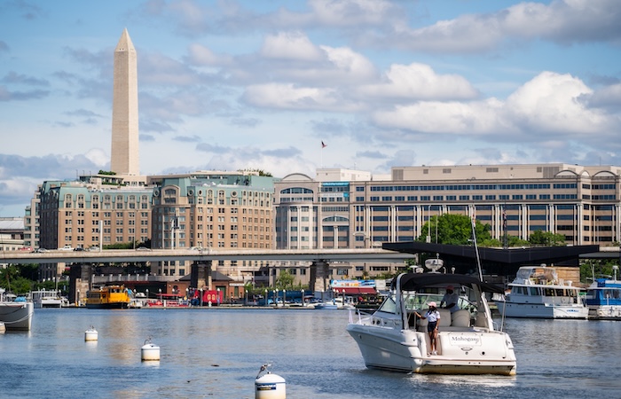 Boats on a calm river with a city skyline and the Washington Monument in the distance.