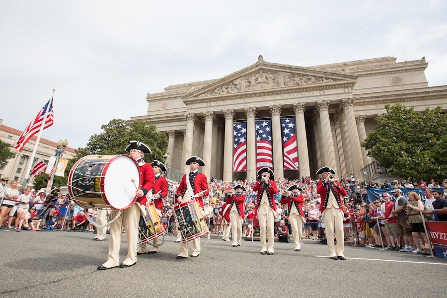 Revolutionary War reenactors with a drum outside a columned building with U.S. flags