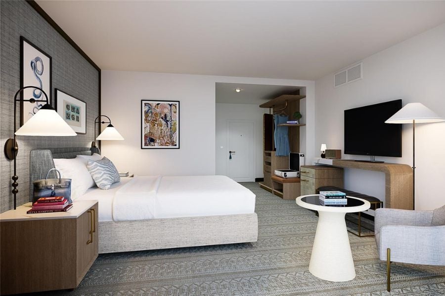 Modern hotel room with bed, TV, lounge chair, and lit lamps