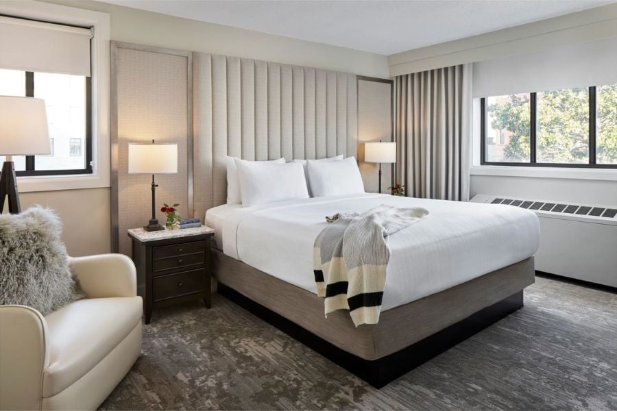 Bright hotel room with king bed, bedside lamps, armchair, and large window