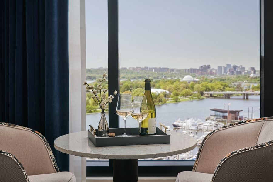 Two armchairs and table with wine, overlooking a sunny river view through a window