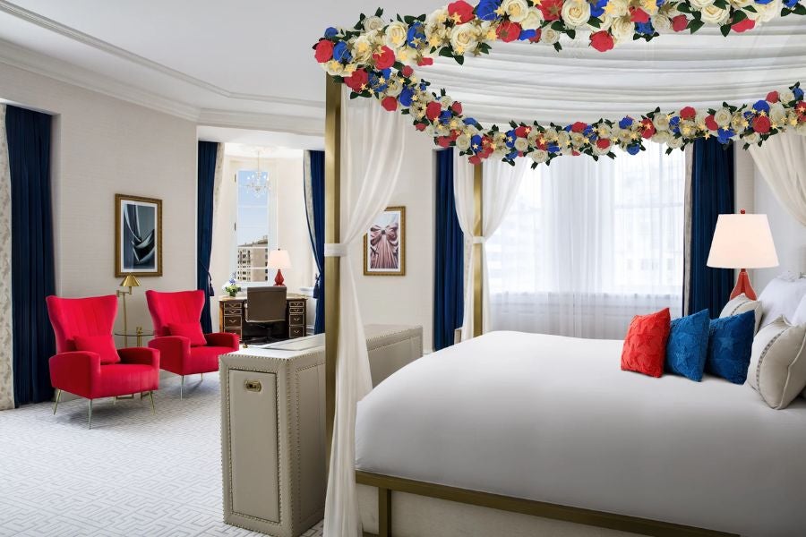 Bright hotel room with king bed, red armchairs, and flower garlands on canopy