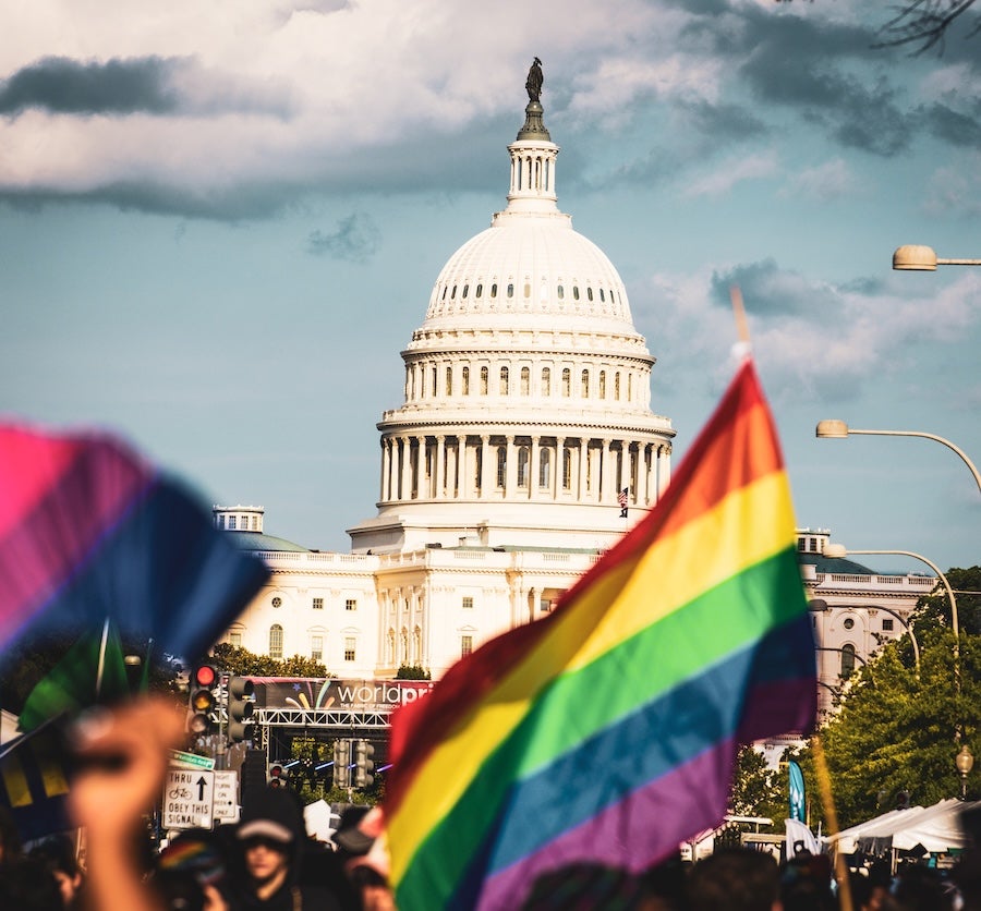 Crowd waving rainbow flags near the U.S. Capitol under a cloudy sky