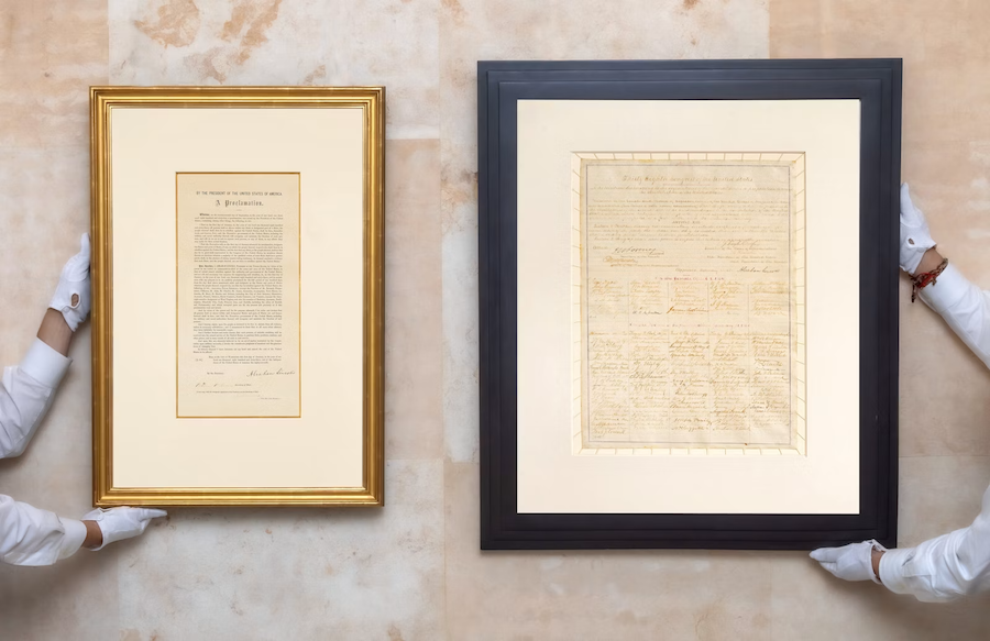 Hands holding two framed documents on a marble surface, one gold frame and one black