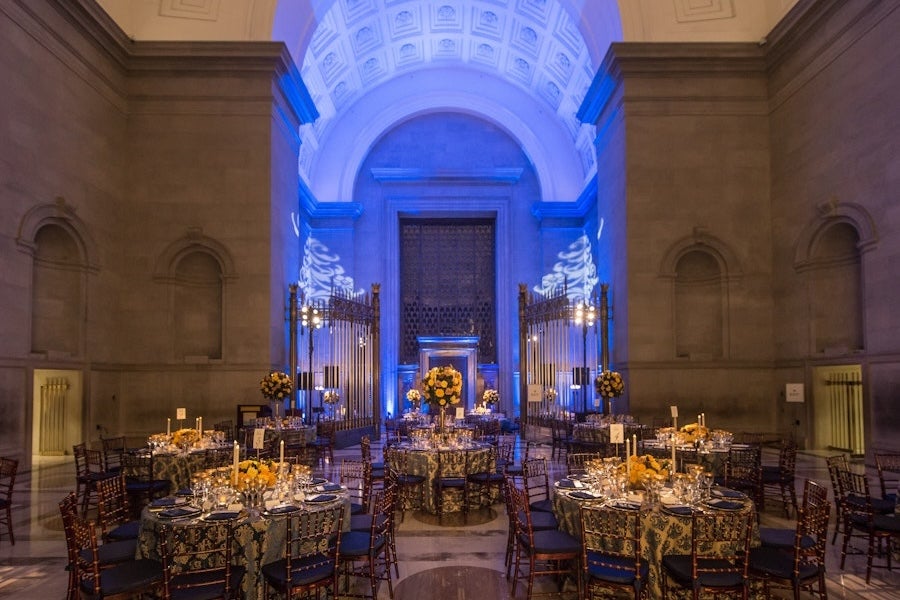 Candlelit dining tables in a grand cathedral hall, blue-lit archway and altar ahead.