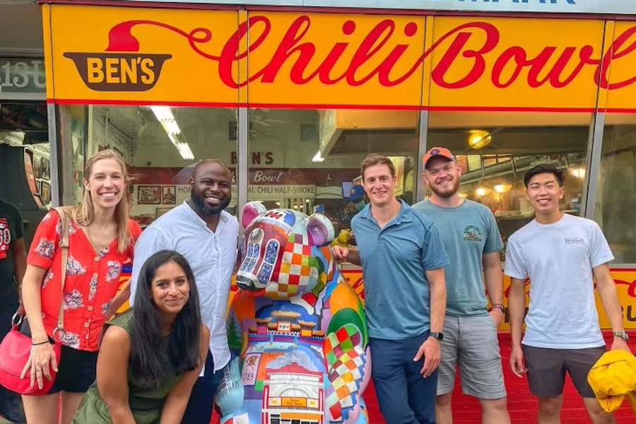 Group of smiling people posing beside a colorful chili bowl statue outside Ben’s Chili Bowl.