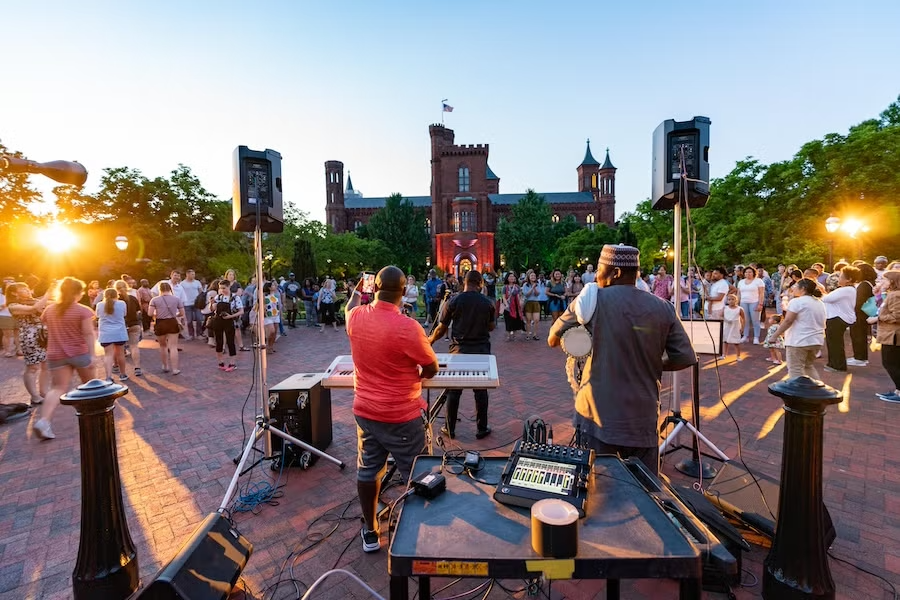 Outdoor concert in a city plaza at sunset, crowd seated facing musicians