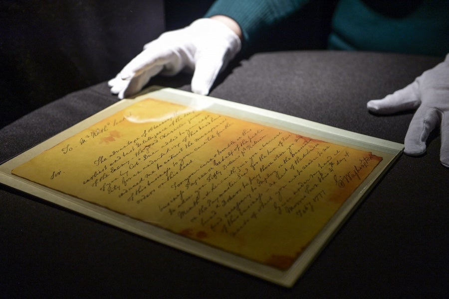 Gloved hands examining a framed yellow document with handwritten text on a dark table