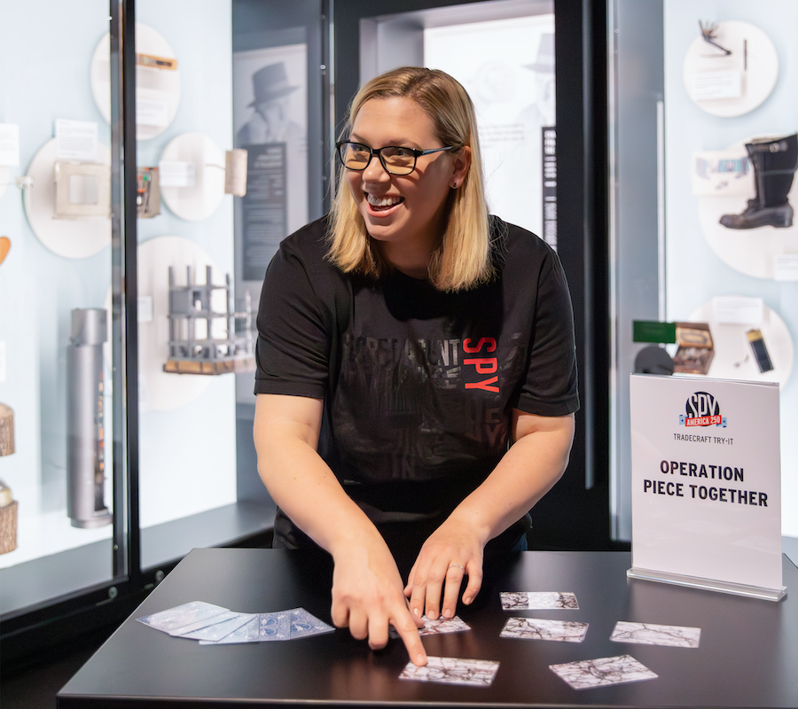 Smiling store employee in black T‑shirt points at display cards on a counter