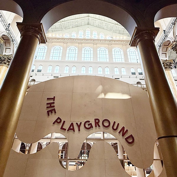Wooden sign for The Playground inside the Great Hall of the National Building Museum under arched windows