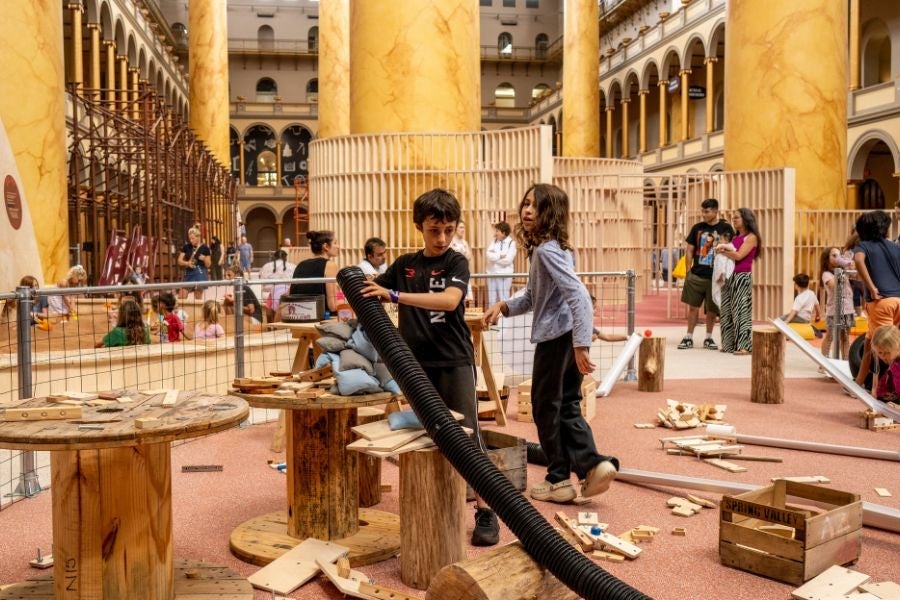 Children building and experimenting with loose materials in a hands-on play area at the National Building Museum’s PLAYGROUND exhibition.