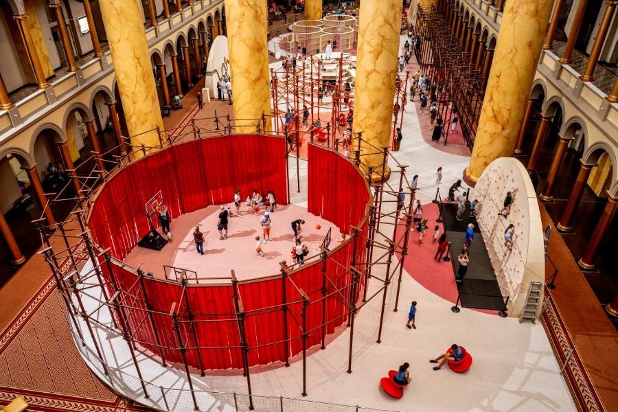 Wide view of the National Building Museum’s Great Hall transformed by the interactive PLAYGROUND exhibition, featuring climbing structures, play areas and hands-on installations.