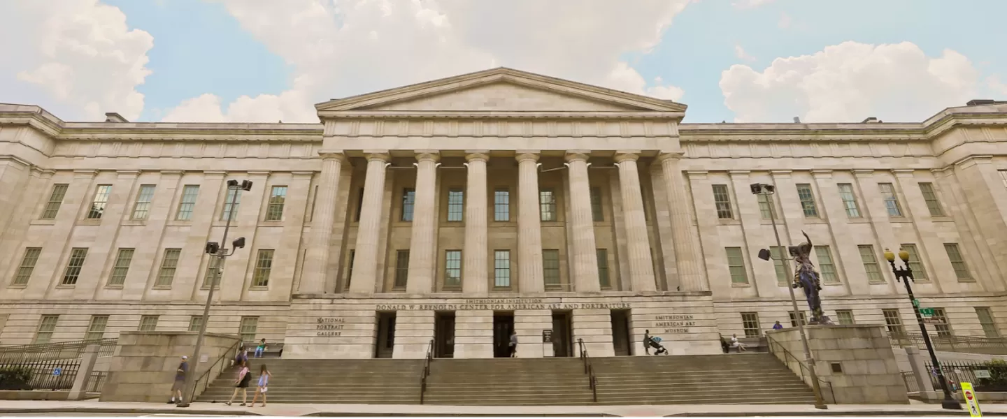 The front facade of the National Portrait Gallery in Washington, DC, with its grand columns and steps leading to the entrance under a partly cloudy sky.